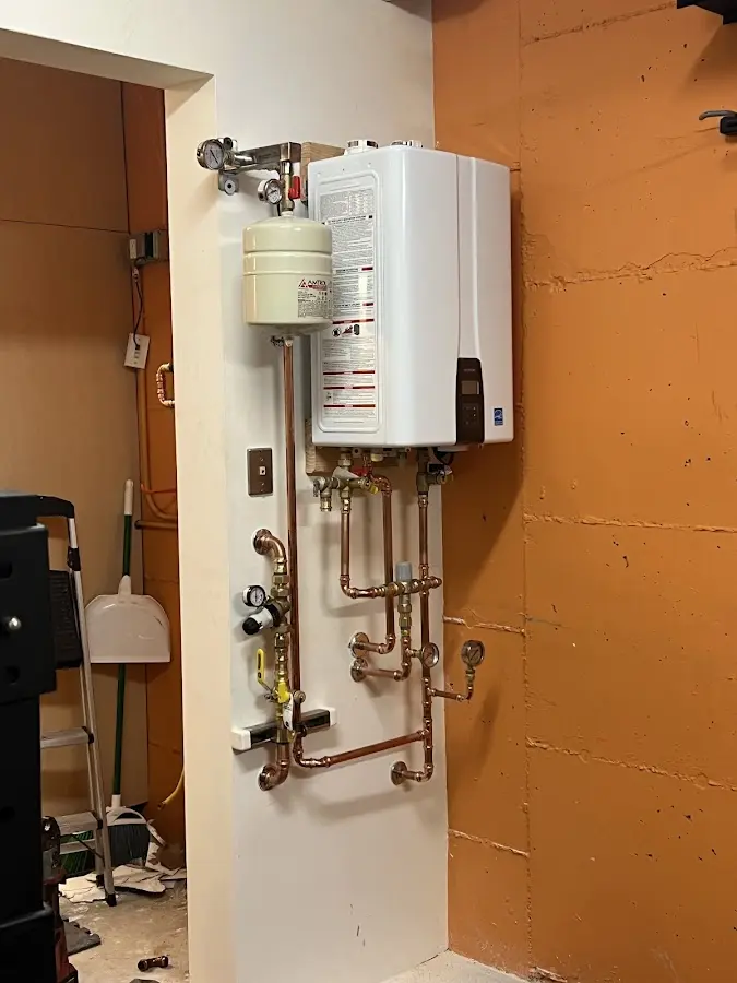 Plumbing technician inspecting water heater connections in Massena